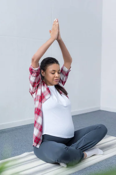 African american pregnant woman meditating with closed eyes and namaste mudra on yoga mat — Stock Photo