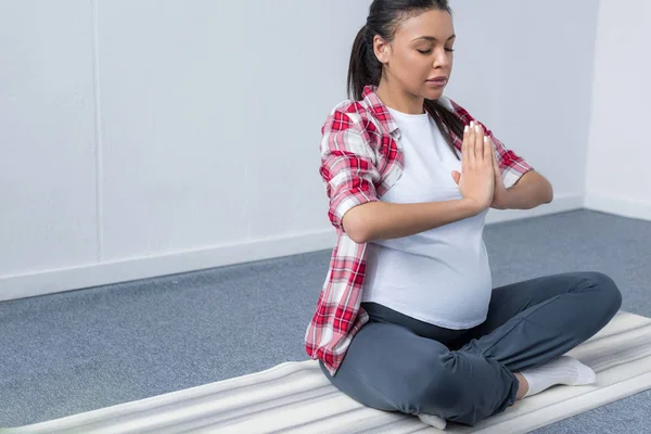 Mujer embarazada afroamericana meditando con namaste mudra en esterilla de yoga - foto de stock