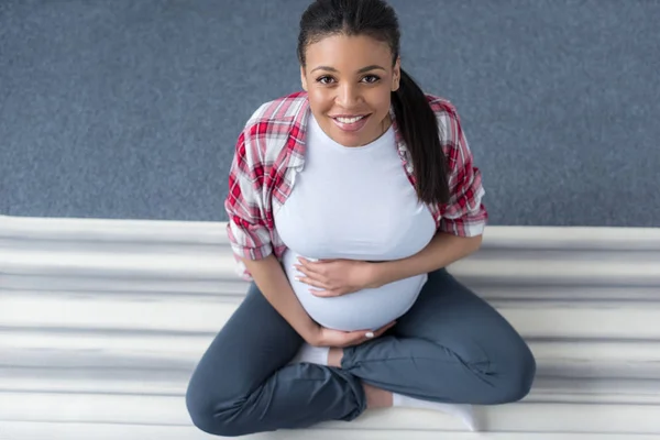 Vista aérea de la sonriente mujer embarazada afroamericana practicando yoga en la estera - foto de stock
