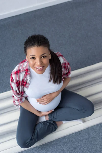 Vista aérea de la sonriente mujer embarazada afroamericana practicando yoga en la estera - foto de stock
