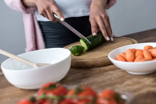 Cropped view of woman cutting cucumber and making salad at kitchen — Stock Photo