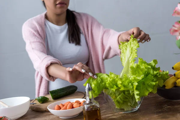 Vista recortada de la mujer embarazada afroamericana haciendo ensalada fresca en la cocina - foto de stock