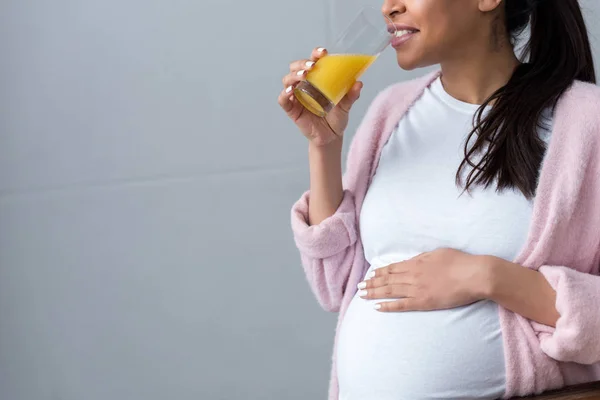 Vista recortada de la mujer embarazada afroamericana bebiendo jugo de naranja - foto de stock