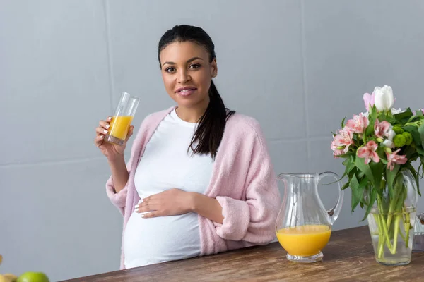 African american pregnant woman with glass of orange juice at kitchen — Stock Photo