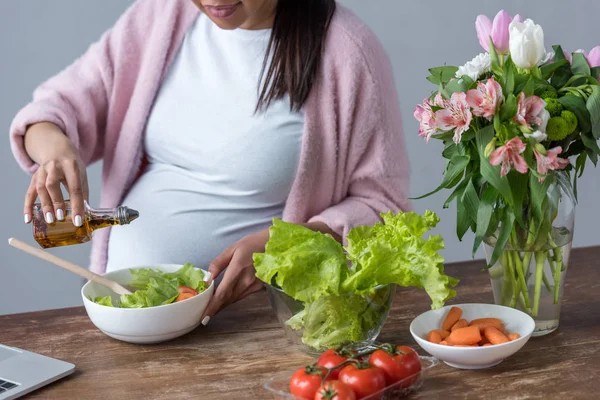 Cropped view of pregnant woman pouring olive oil into salad at kitchen — Stock Photo