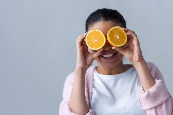 Cheerful african american girl with halves of orange, isolated on grey — Stock Photo