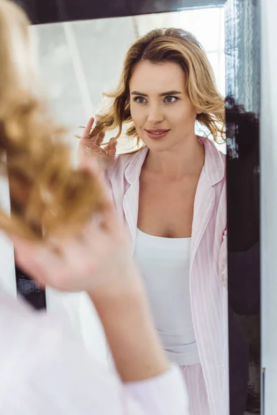 Femme blonde en pyjama regardant son reflet dans le miroir — Photo de stock