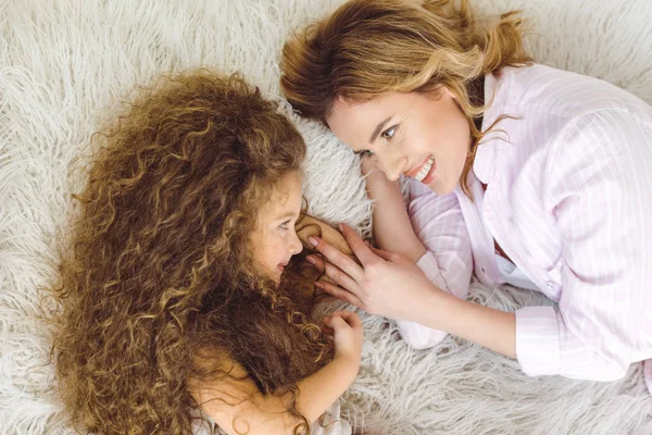 Vue du dessus de la mère heureuse et adorable fille bouclée couchée sur une couverture en peau de mouton — Photo de stock