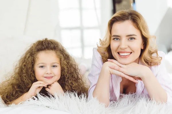 Smiling mom and adorable curly daughter lying and looking at camera — Stock Photo