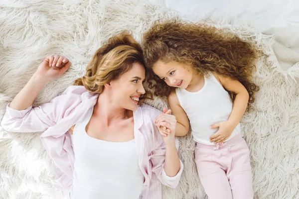 Top view of smiling mom and curly daughter relaxing and looking at each other — Stock Photo