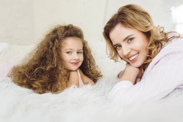 Mère et fille souriantes allongées sur une couverture en peau de mouton et regardant la caméra — Photo de stock