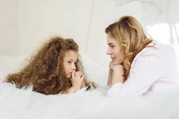 Beautiful mother and pensive daughter lying on sheep skin blanket — Stock Photo