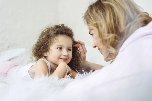 Feliz madre y adorable hija rizada acostada en piel de oveja manta - foto de stock