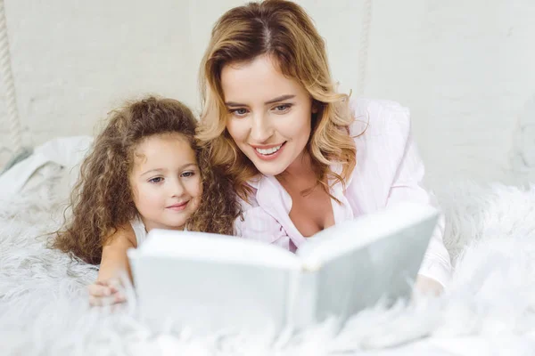 Mother and curly daughter reading book together — Stock Photo