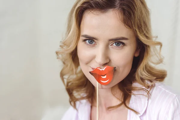 Funny woman in pajamas holding red paper lips on stick — Stock Photo