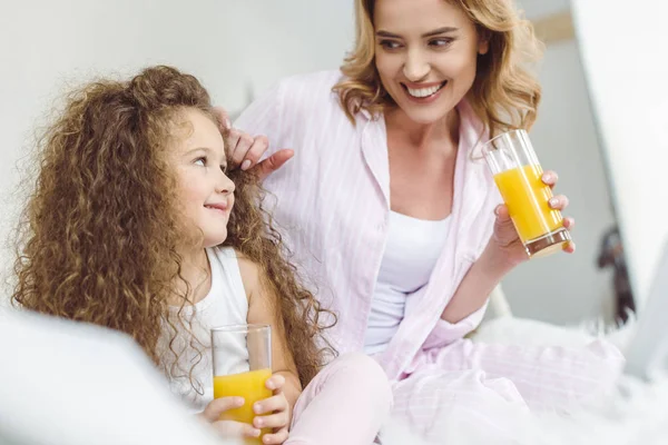 Mãe feliz e filha encaracolada com copos de suco de laranja — Fotografia de Stock