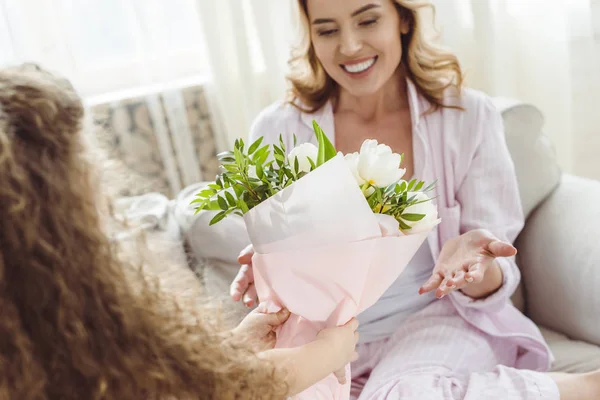 Fille présentant bouquet de fleurs à sa maman souriante le jour de la fête des mères heureuses — Photo de stock