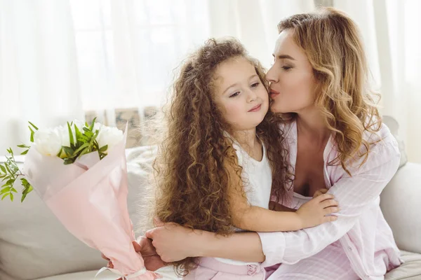 Glückliche Mutter küsst ihre Tochter und hält Blumenstrauß für einen glücklichen Muttertag — Stockfoto