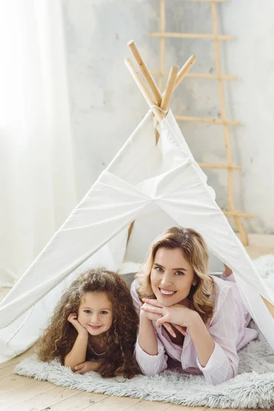 Belle mère gaie et fille bouclée couché dans enfant wigwam — Photo de stock