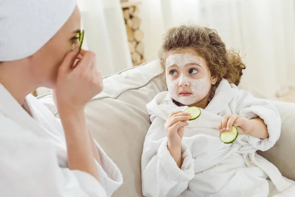 Madre e hija con rodajas de pepino haciendo mascarilla facial - foto de stock