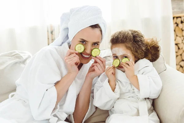 Feliz madre e hija con rodajas de pepino haciendo procedimientos cosméticos - foto de stock