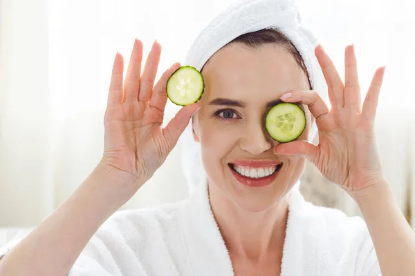 Mujer sonriente sosteniendo rodajas de pepino en los ojos - foto de stock