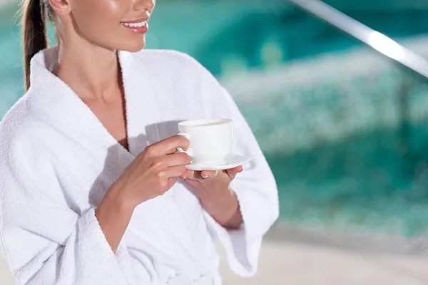 Abgeschnittene Aufnahme eines lächelnden Mädchens im Bademantel mit einer Tasse Kaffee im Kurzentrum — Stockfoto