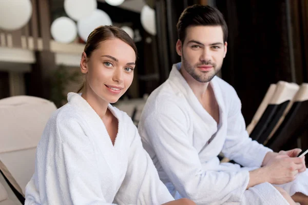 Hermosa pareja joven en albornoces sonriendo a la cámara en el centro de spa - foto de stock