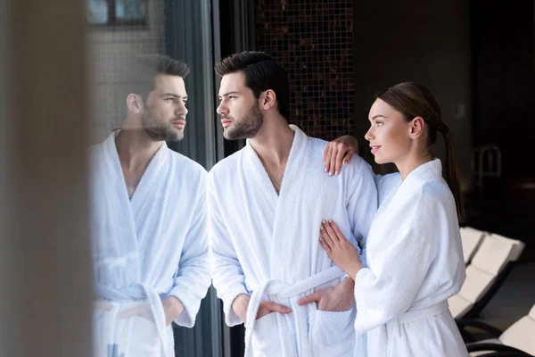 Young couple in bathrobes standing together and looking away in spa center — Stock Photo