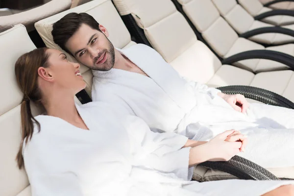 Junges Paar in Bademänteln lächelnd einander beim Ausruhen im Wellness-Center — Stockfoto