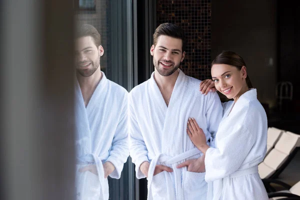 Happy young couple in bathrobes smiling at camera in spa center — Stock Photo