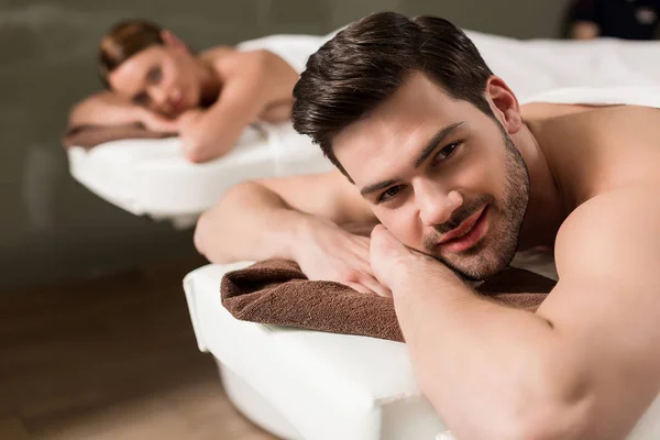 Handsome young man looking at camera while having massage in spa salon — Stock Photo