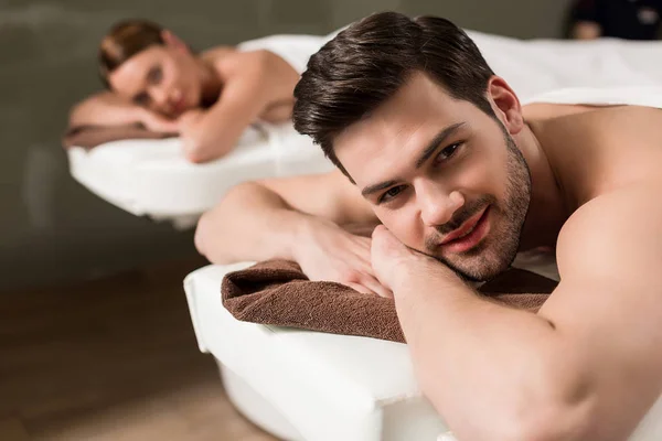 Joven guapo mirando a la cámara mientras tiene masaje en el salón de spa - foto de stock