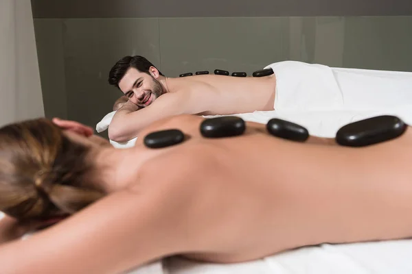 Enfoque selectivo de la pareja mirándose mientras se hace masajes con piedras calientes en el centro de spa — Stock Photo