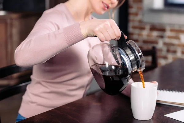 Visão parcial da mulher derramando café na xícara na mesa em casa — Fotografia de Stock