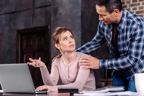 Mann feuert verärgerte Frau zu Hause mit Laptop am Tisch an, finanzielle Probleme — Stockfoto