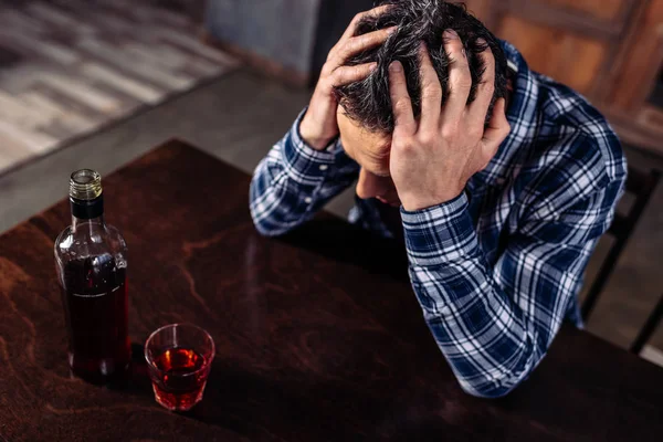 High angle view of drunk man sitting at table with bottle and glass of alcohol at home — Stock Photo