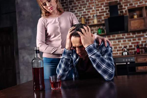 Пьяный мужчина сидит за столом, пока жена стоит рядом с домом — стоковое фото