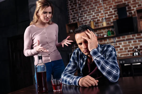 Пьяный мужчина сидит за столом, ссорясь с женой, стоящей рядом с домом — стоковое фото