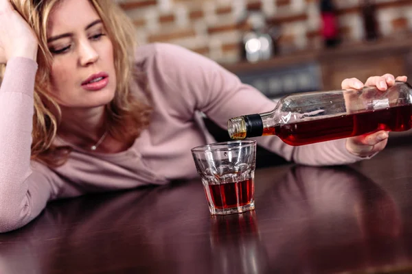 Mujer vertiendo alcohol en el vidrio mientras está sentado en la mesa en la cocina - foto de stock