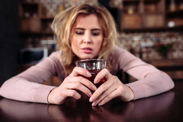 Retrato de mulher bêbada com copo de álcool sentado t mesa em casa — Fotografia de Stock