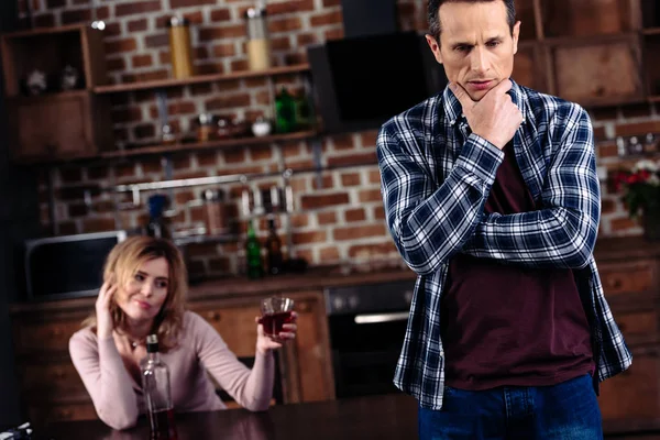 Selective focus of pensive man and drunk wife at table in kitchen at home — Stock Photo