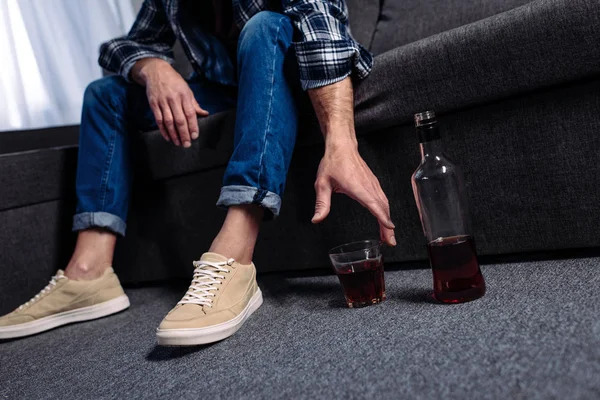 Visão parcial do homem que toma bebida alcoólica enquanto está sentado no sofá em casa — Fotografia de Stock