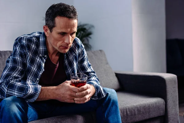 Vista lateral del hombre con vaso de alcohol sentado en el sofá en casa - foto de stock