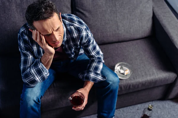 Vista de ángulo alto del hombre con vaso de bebida sentado en el sofá - foto de stock