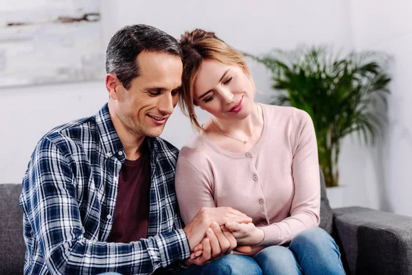 Wife and husband holding hands while resting on sofa at home — Stock Photo