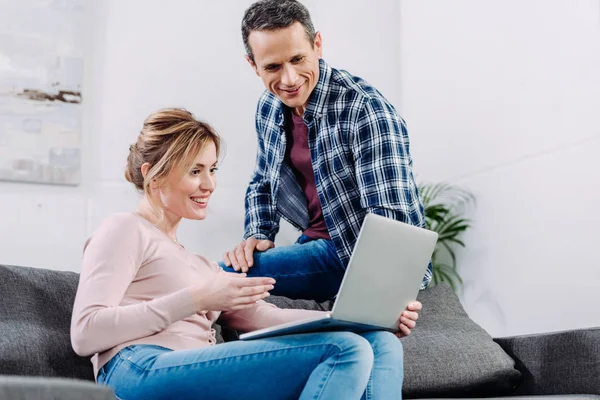 Smiling couple using laptop on sofa at home — Stock Photo