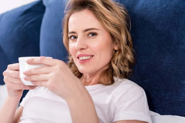 Портрет улыбающейся женщины с чашкой кофе в постели — стоковое фото