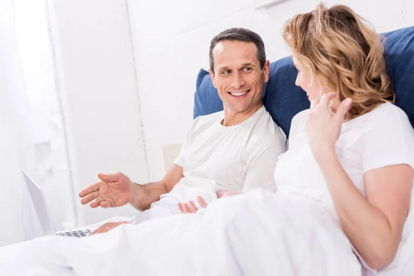Smiling couple with laptop in bed at home — Stock Photo