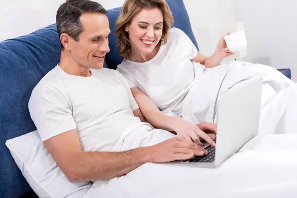 Портрет усміхненої пари з ноутбуком в ліжку вдома — стокове фото